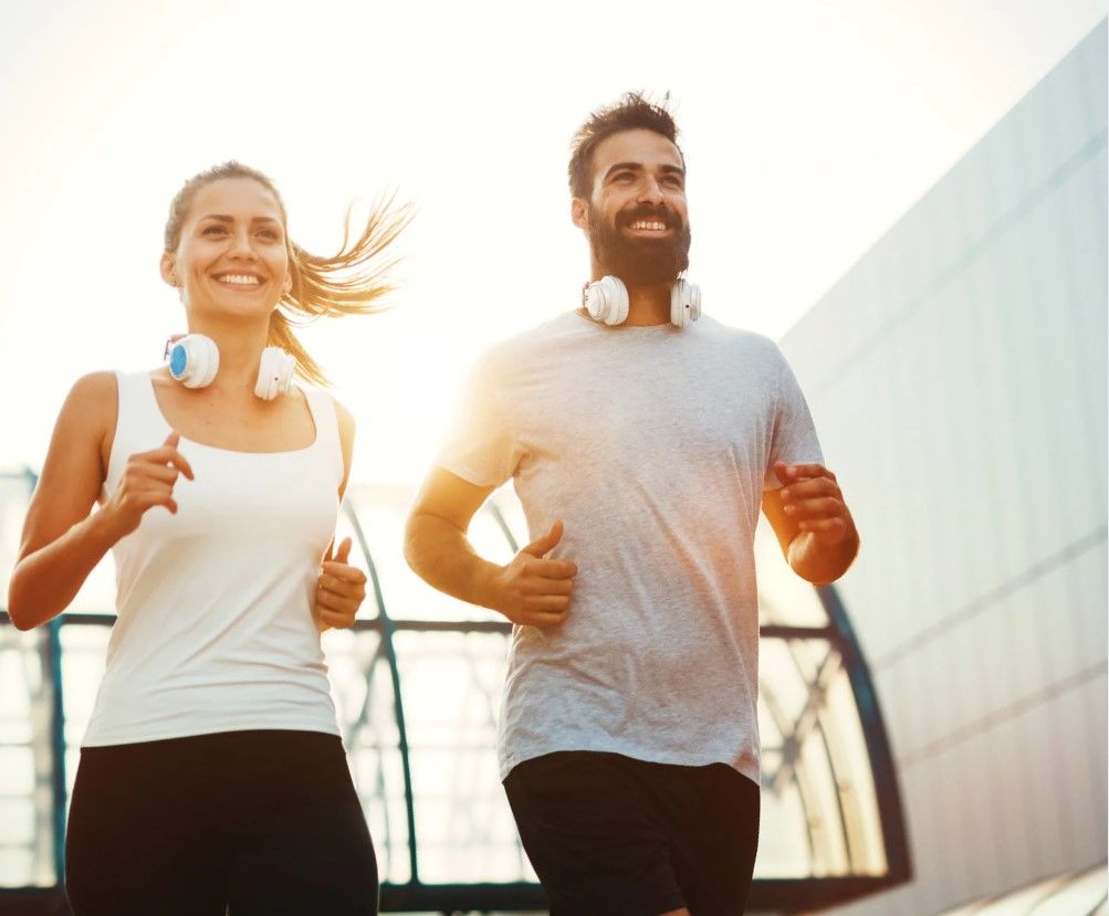 Couple jogging outdoors with headphones at sunset.