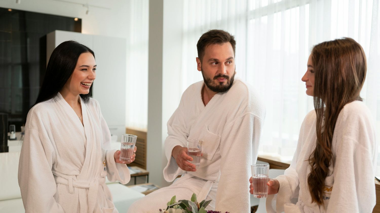 Friends enjoying drinks in spa robes.